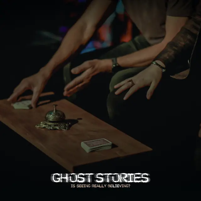 Hands hovering over a séance table with a brass bell and a deck of cards